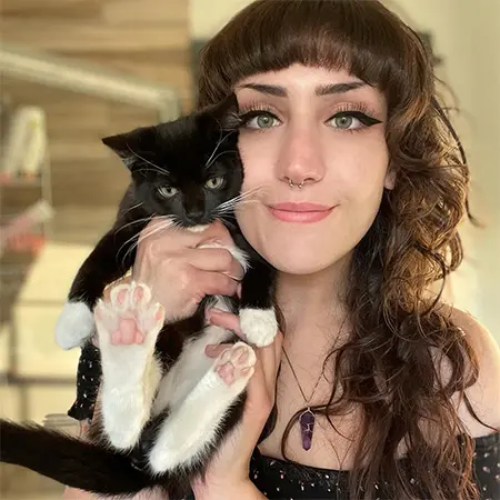 Young woman holding a black and white cat, both looking at the camera.
