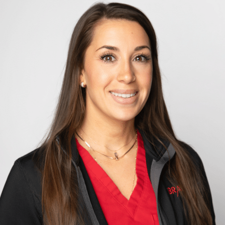 A woman with long brown hair, wearing a red top and black jacket, smiles at the camera.